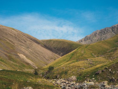Free Captured under a bright blue sky, this picturesque mountain valley features rolling hills and a rocky foreground. Stock Photo