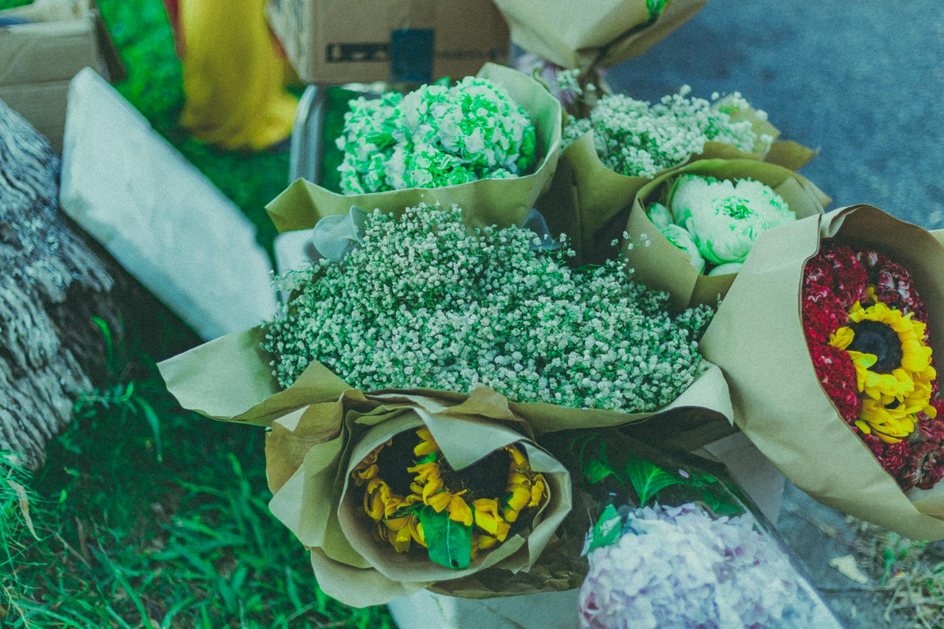 Vibrant flower bouquets wrapped in kraft paper displayed outdoors, featuring sunflowers, baby's breath, and more.