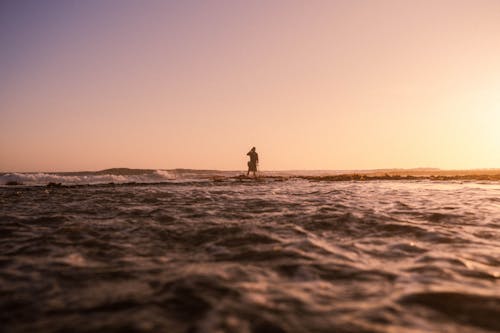 Person Standing in Shallow Sea at Sunrise