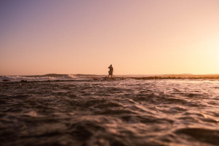 Person Standing In Shallow Sea At Sunrise