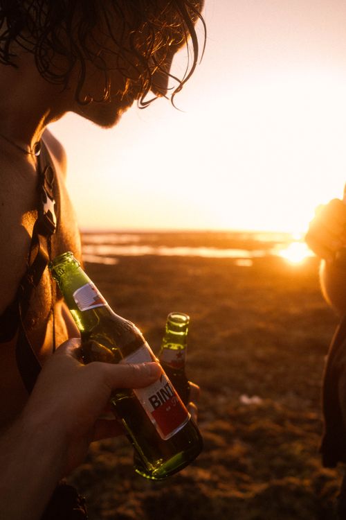 Free Relaxing beach sunset with people holding beer, enjoying vacation vibes. Stock Photo