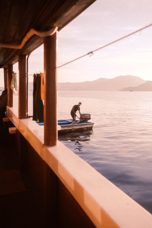 Free A man stands on a motorboat in the ocean at sunrise surrounded by mist and mountains. Stock Photo