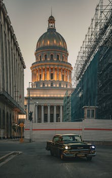 Classic vintage car in front of El Capitolio in Havana at dusk with scaffolding on street.