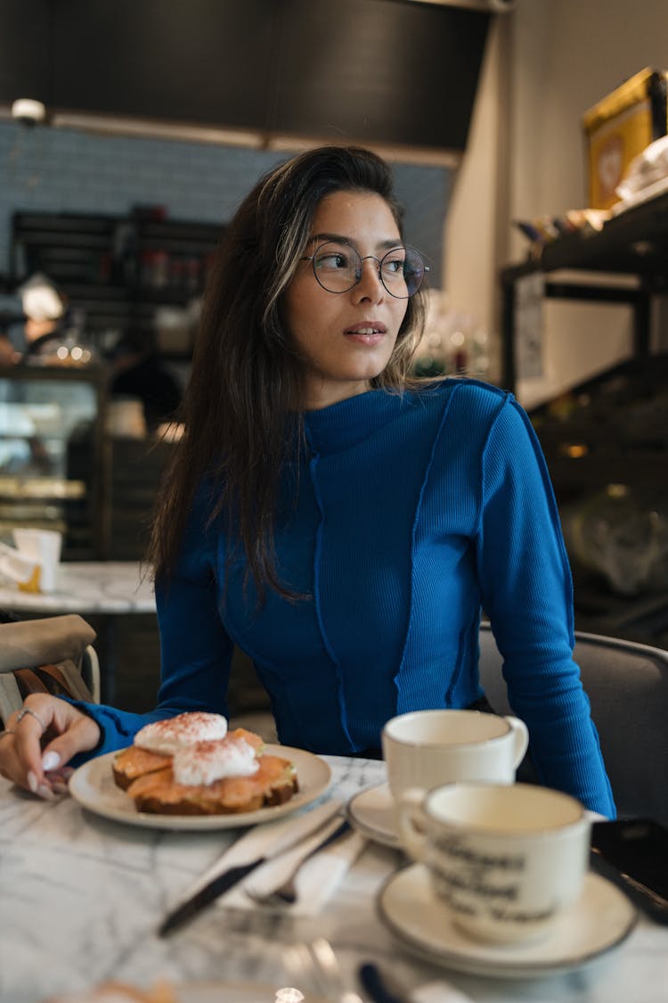 Woman In Blue Dress Sitting At Table In Restaurant