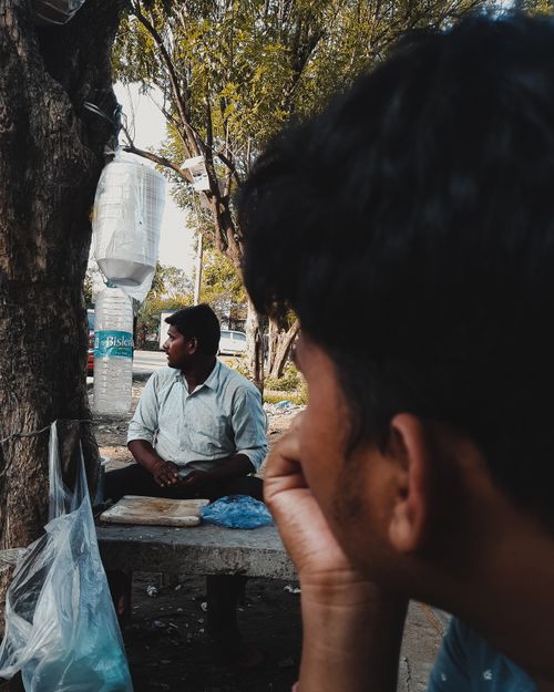 Free A candid shot of two men in conversation by a tree in a city environment. Captured outdoors. Stock Photo
