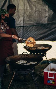 Cooks preparing traditional pancakes outdoors at a Honolulu food festival.
