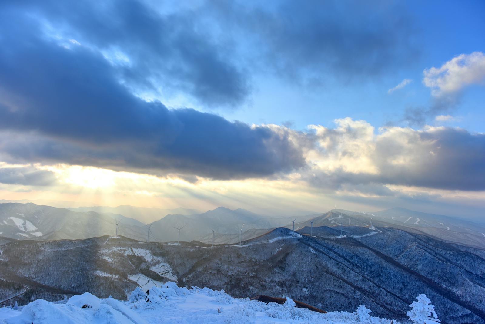 Parco eolico su cresta montana innevata con turbine in fila