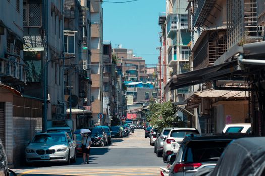 A vibrant city street lined with residential buildings and parked cars under a clear blue sky.
