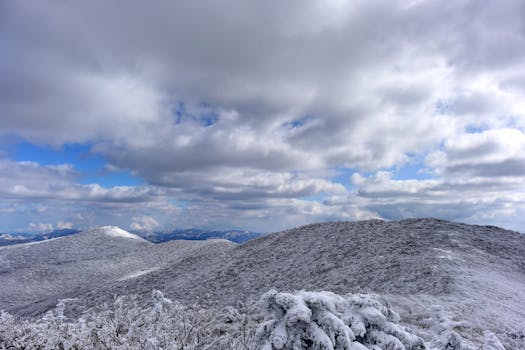 Scenic winter landscape with snow-covered mountains under a dramatic cloudy sky.