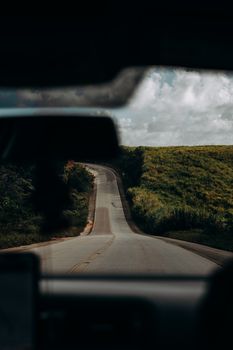 A winding road through lush green landscapes in Jequiá da Praia, Brazil, under a cloudy sky.