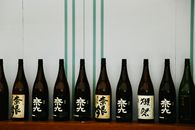 A row of Japanese sake bottles displayed on a wooden shelf against a decorative backdrop.