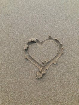 A close-up of a heart shape drawn on sandy beach surface, capturing natural texture.