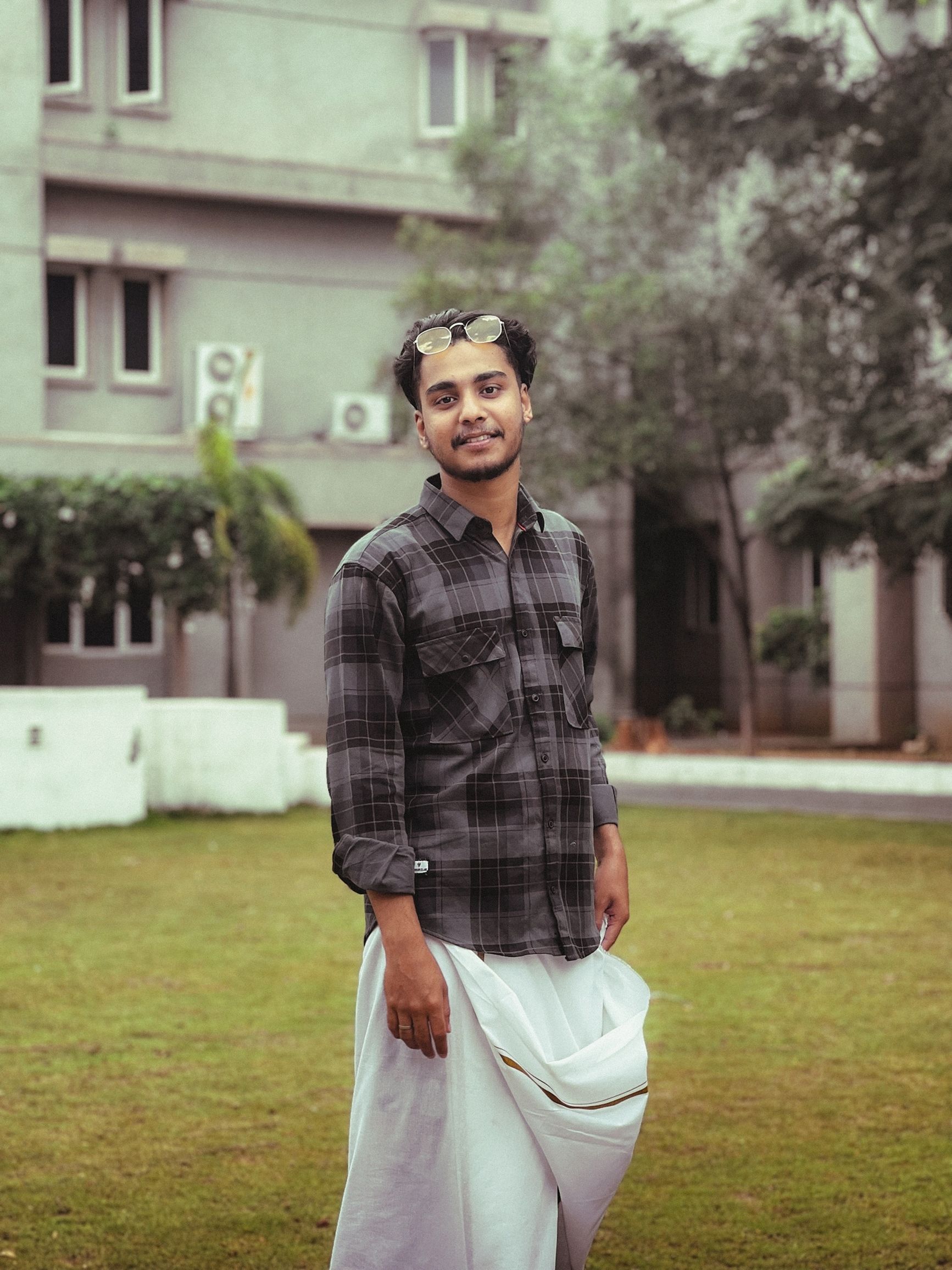 Smiling man in traditional attire standing outdoors in urban India.