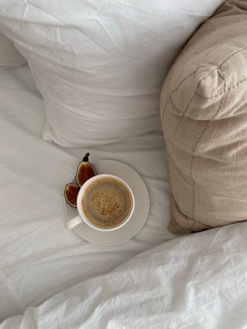 A cozy scene with a cup of coffee and fresh figs on a bed, creating a relaxing morning vibe.
