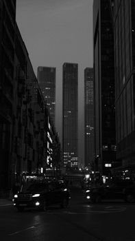 Black and white urban scene with towering skyscrapers and city lights at night.