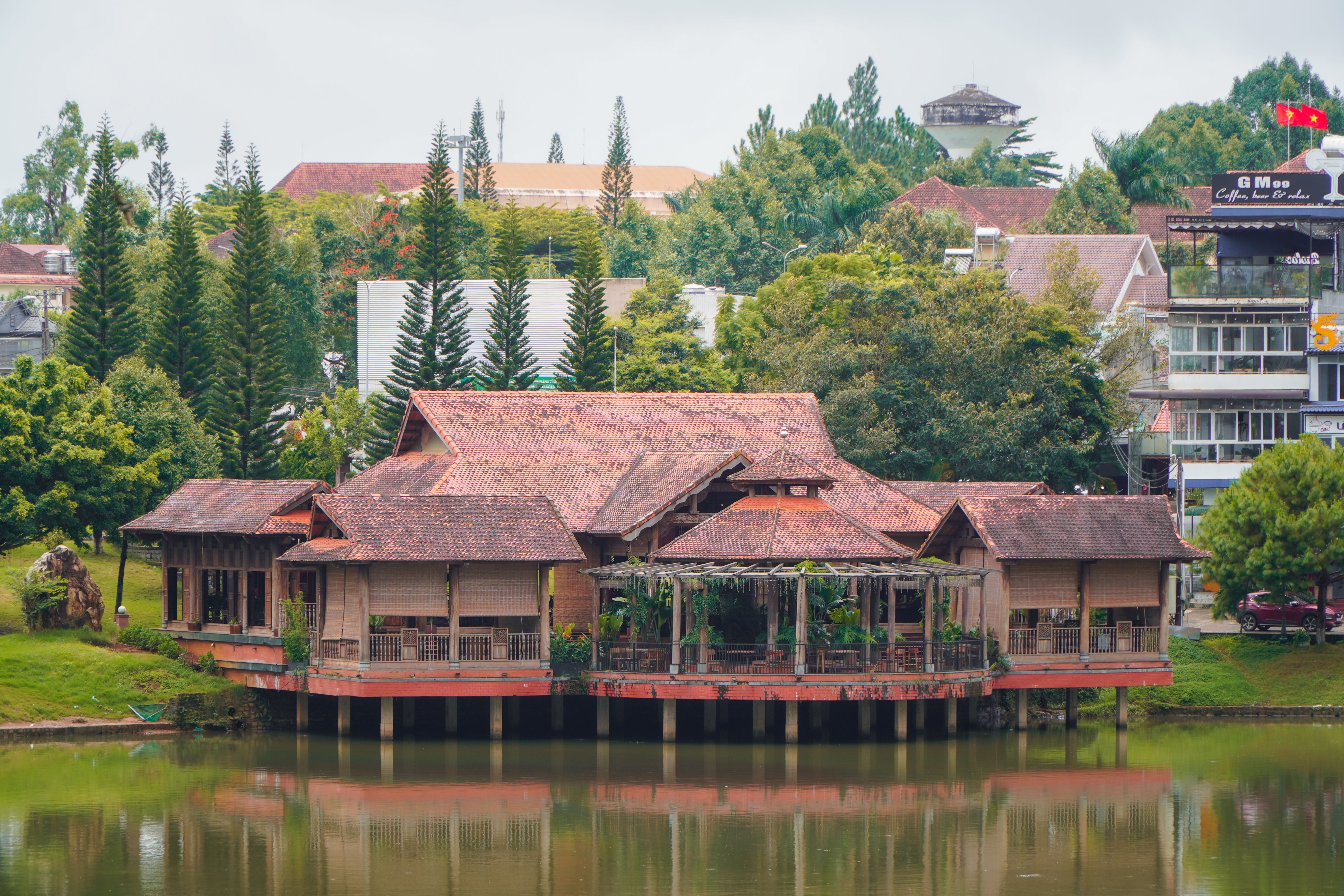 Scenic view of a traditional Vietnamese wooden structure by a tranquil lake surrounded by greenery.