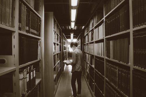 Man among Shelves with Books in Library
