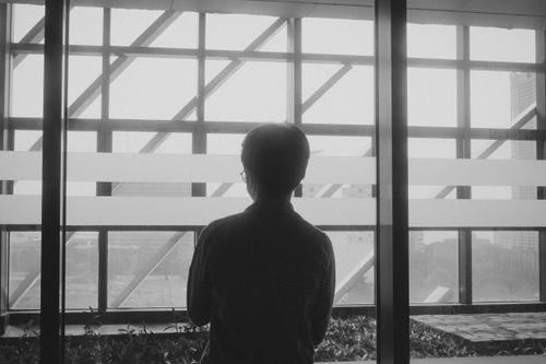 Free Black and white silhouette of a man gazing out of a modern glass window Stock Photo