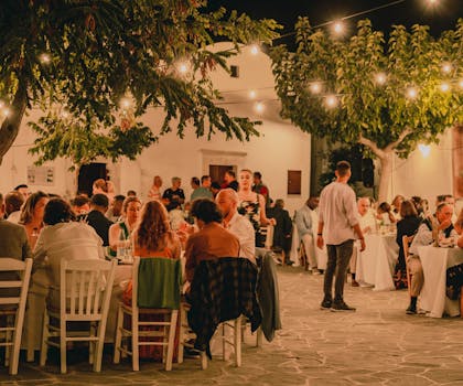 A vibrant outdoor dinner gathering with people dining under string lights, creating a festive atmosphere.
