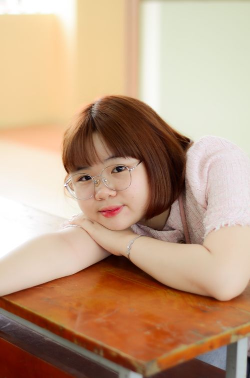Free Young student resting her chin on a classroom desk, wearing glasses. Stock Photo
