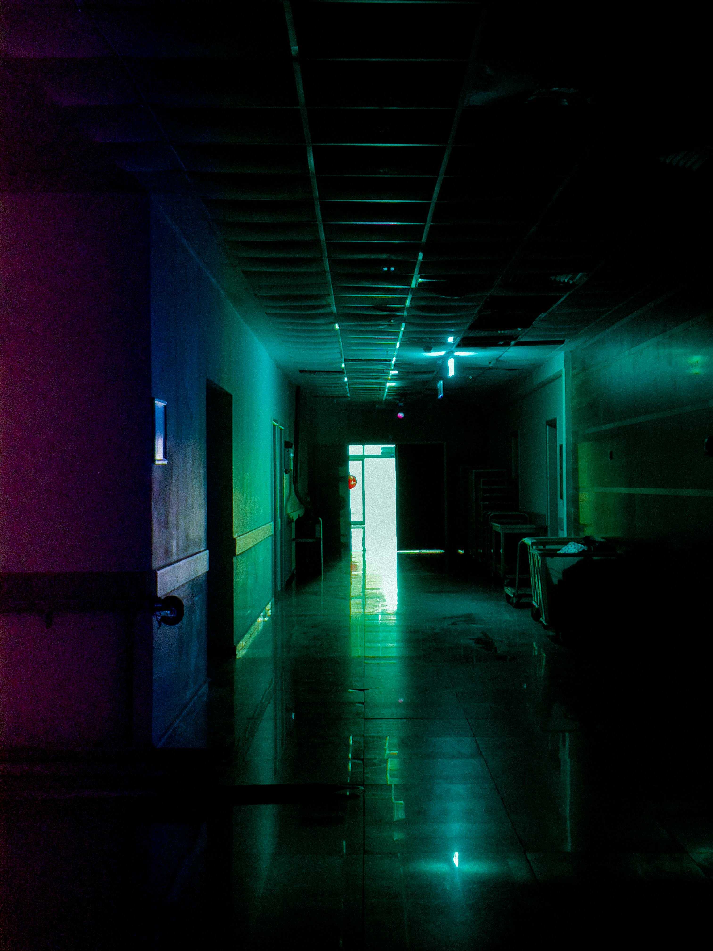 A long dark hospital corridor with pale green light glowing at the far end, creating a sense of depth and unease.