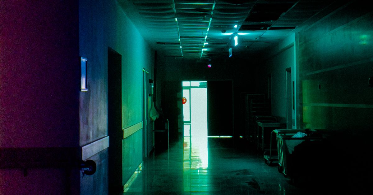 A long dark hospital corridor with pale green light glowing at the far end, creating a sense of depth and unease.