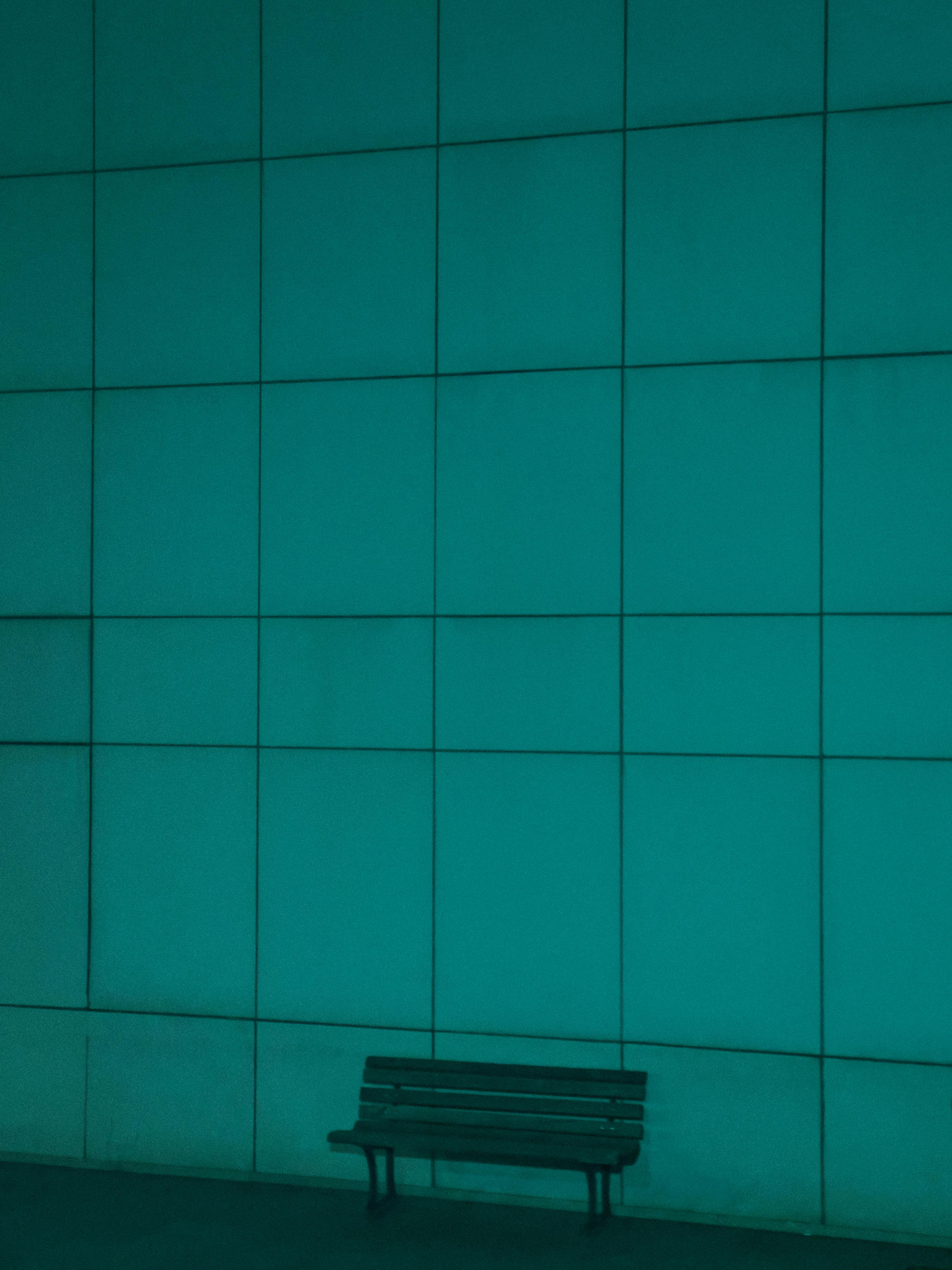 A minimalist photo featuring a bench against a large green geometric wall, offering ample copyspace.