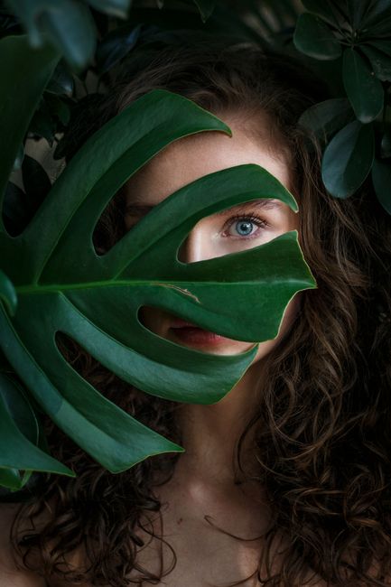 A beautiful woman peeks through lush green leaves in this captivating portrait.