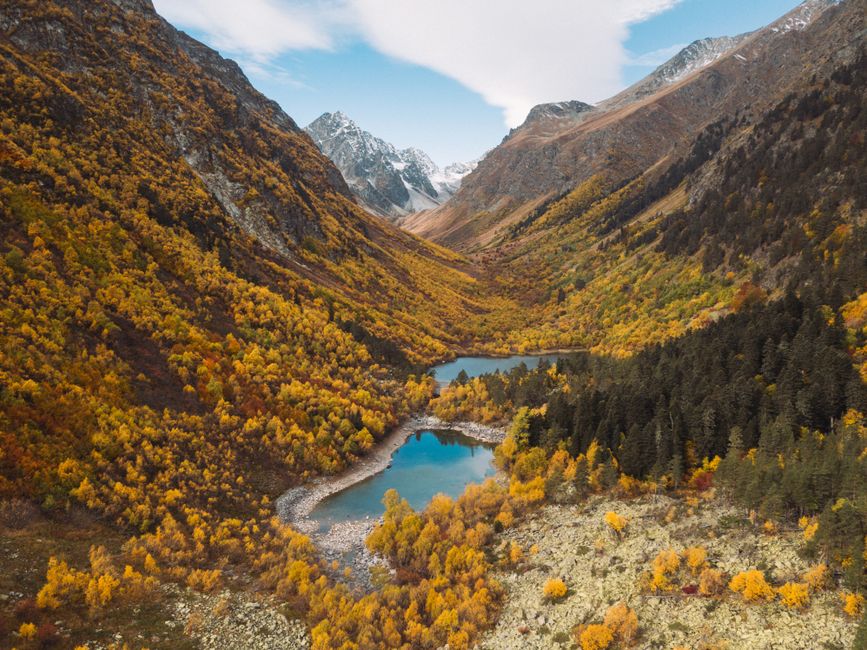 Vibrant autumn colors in a mountain valley with clear lakes and snow-capped peaks.