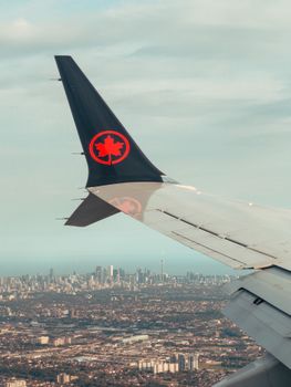 Aerial view from airplane window showing Toronto skyline and airplane wing.