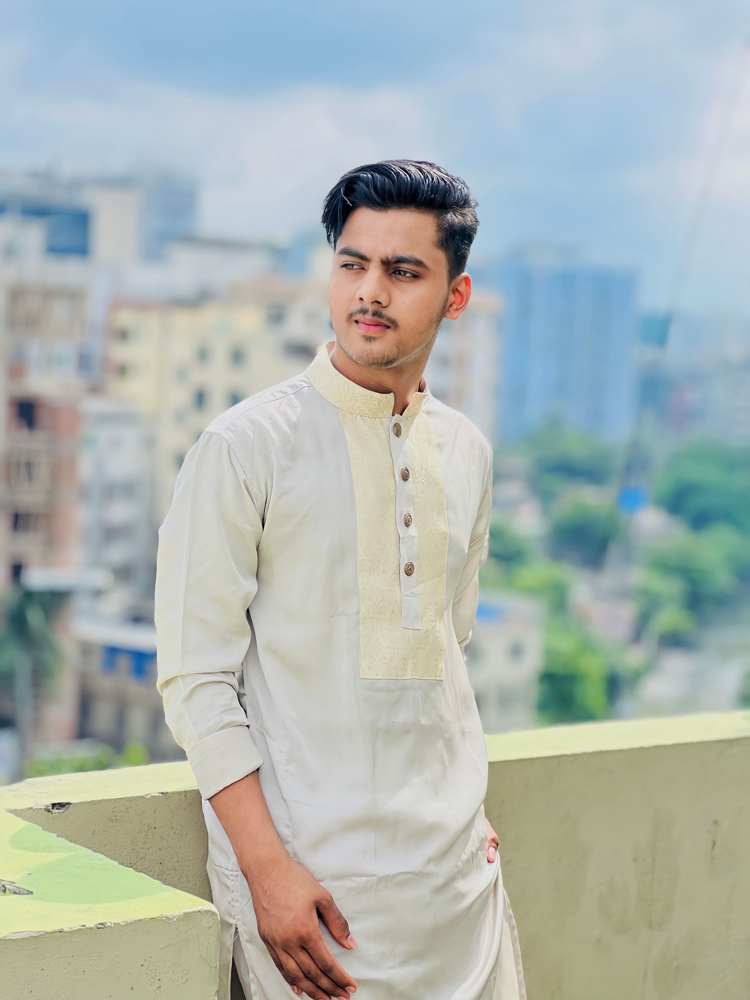 Man in traditional attire standing on a rooftop with cityscape background.