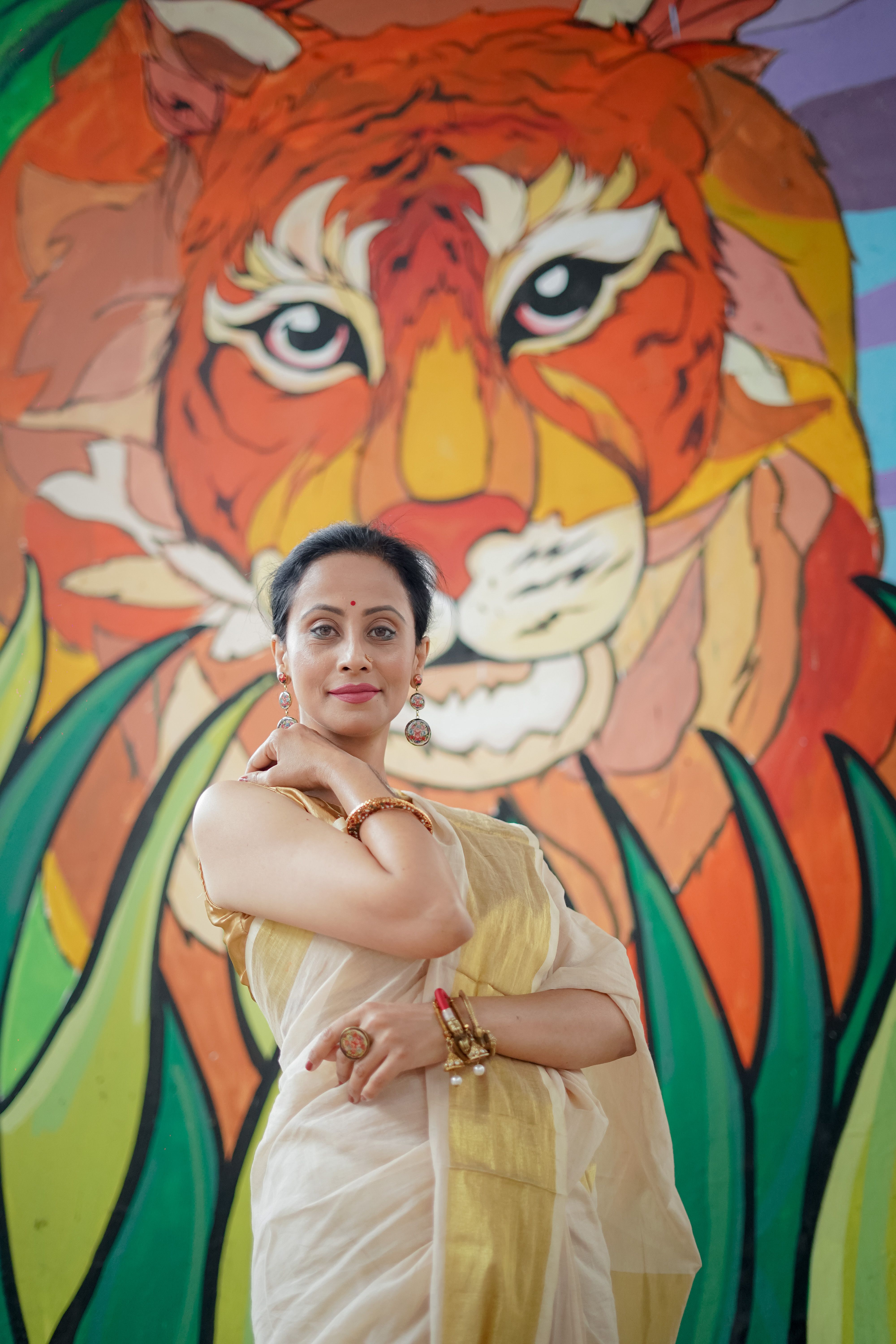 Elegant portrait of a South Asian woman in a saree posing confidently in front of a vibrant tiger mural.