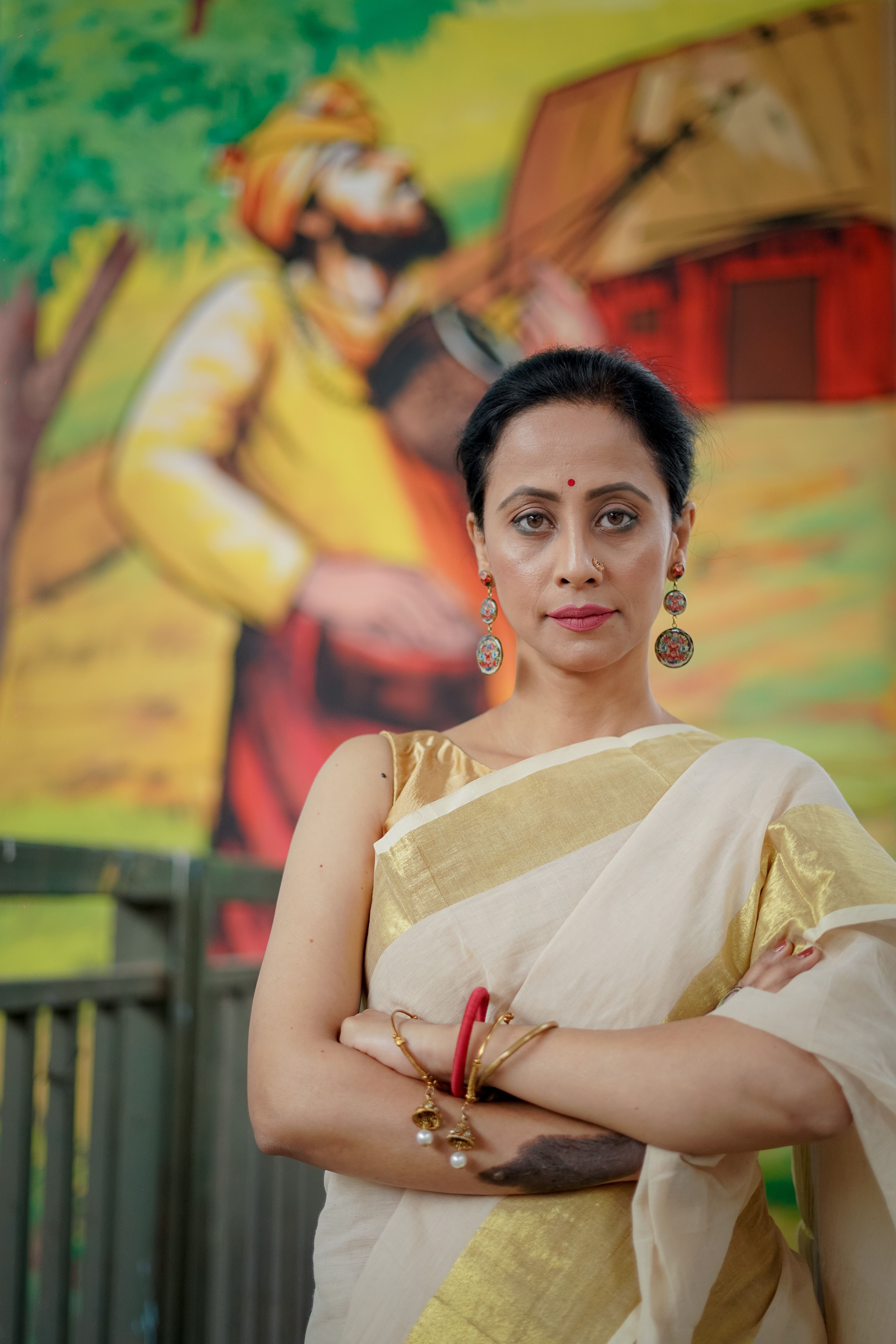 Elegant Indian woman in traditional saree poses confidently in front of a colorful mural, showcasing cultural essence.