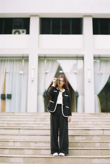 Stylish young woman with camera standing on steps in front of modern building.