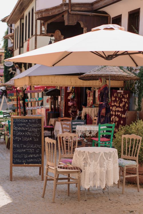 Free A picturesque outdoor café with vintage chairs and umbrellas, nestled in a historic town setting. Stock Photo