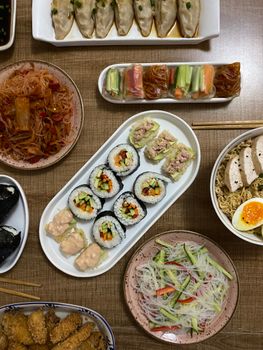 Top view of a variety of Asian dishes including sushi, dumplings, and noodles on a table.