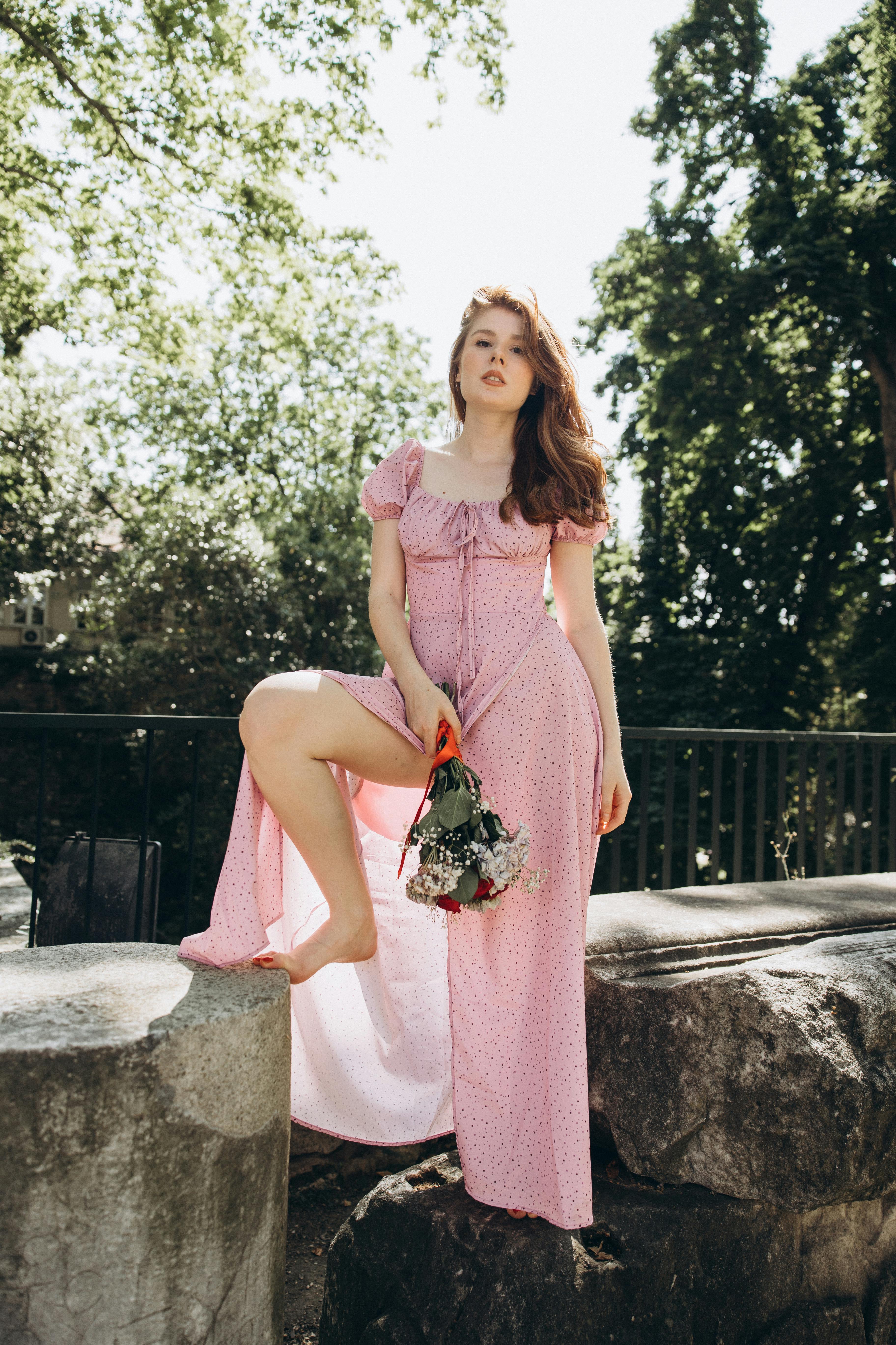 a woman in a pink dress sitting on a rock