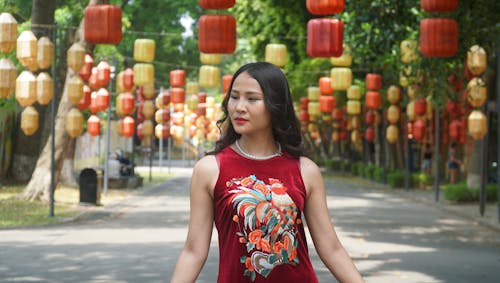 Young Woman in a Red Dress Posing in a Park Decorated with Lanterns