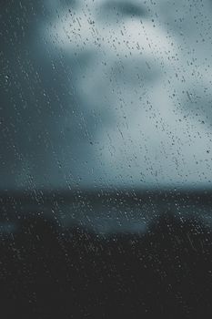 Raindrops trickle down a window, creating a moody and atmospheric view.