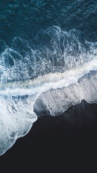 Stunning aerial view of ocean waves crashing onto the shore with vibrant blue hues and white foamy surf.