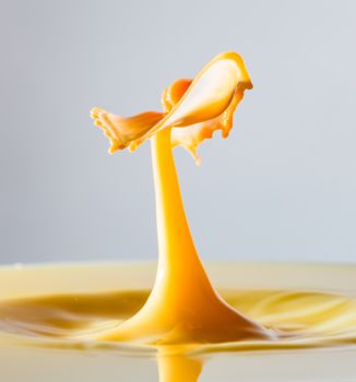 Close-up of a vibrant yellow liquid splash captured in motion against a gray background.