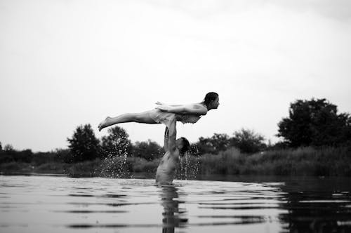 Shirtless Man Standing Waist deep in a Lake Holding aloft a Woman