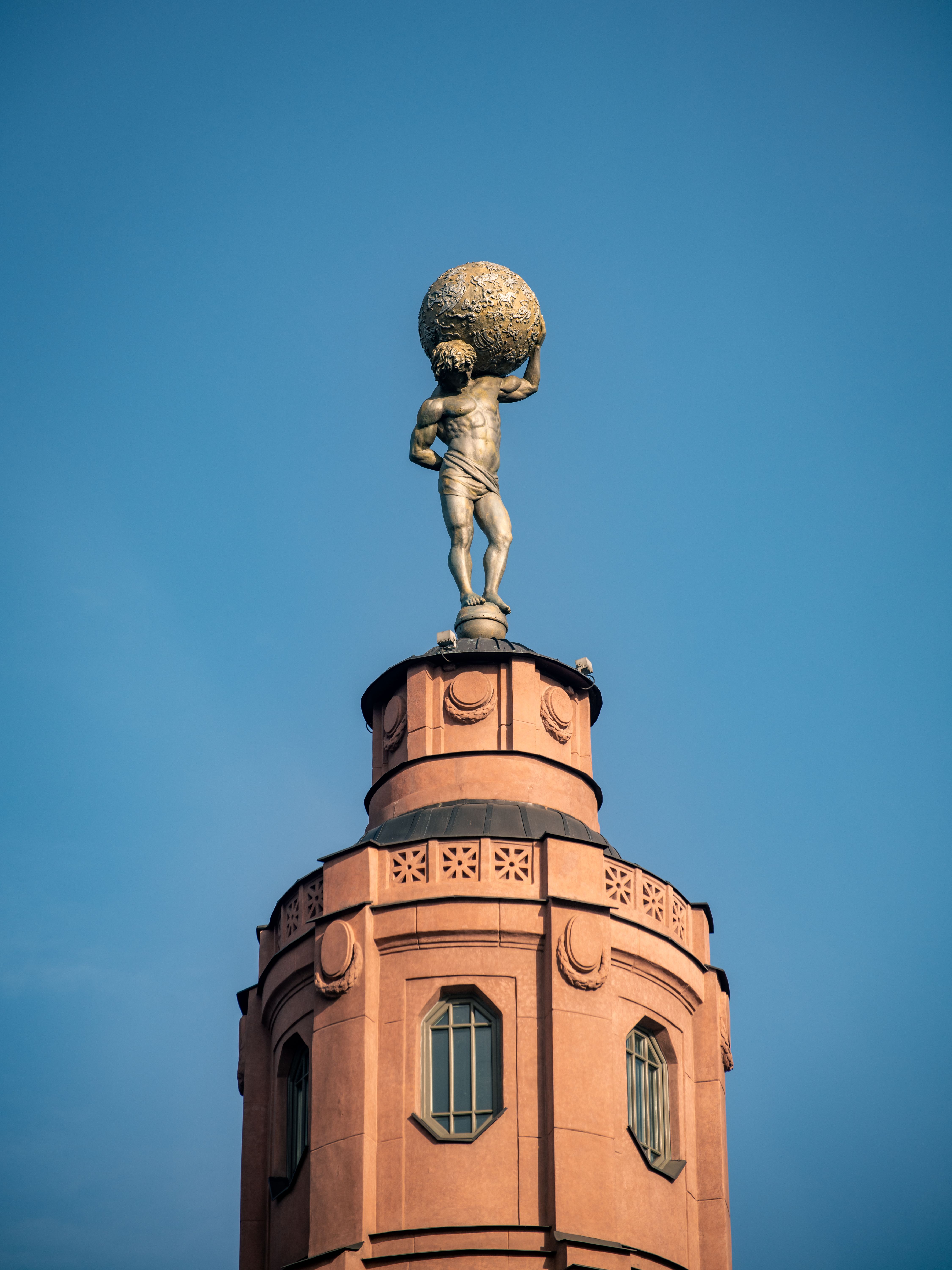 Atlas statue atop a historic Vilnius building tower against clear sky.