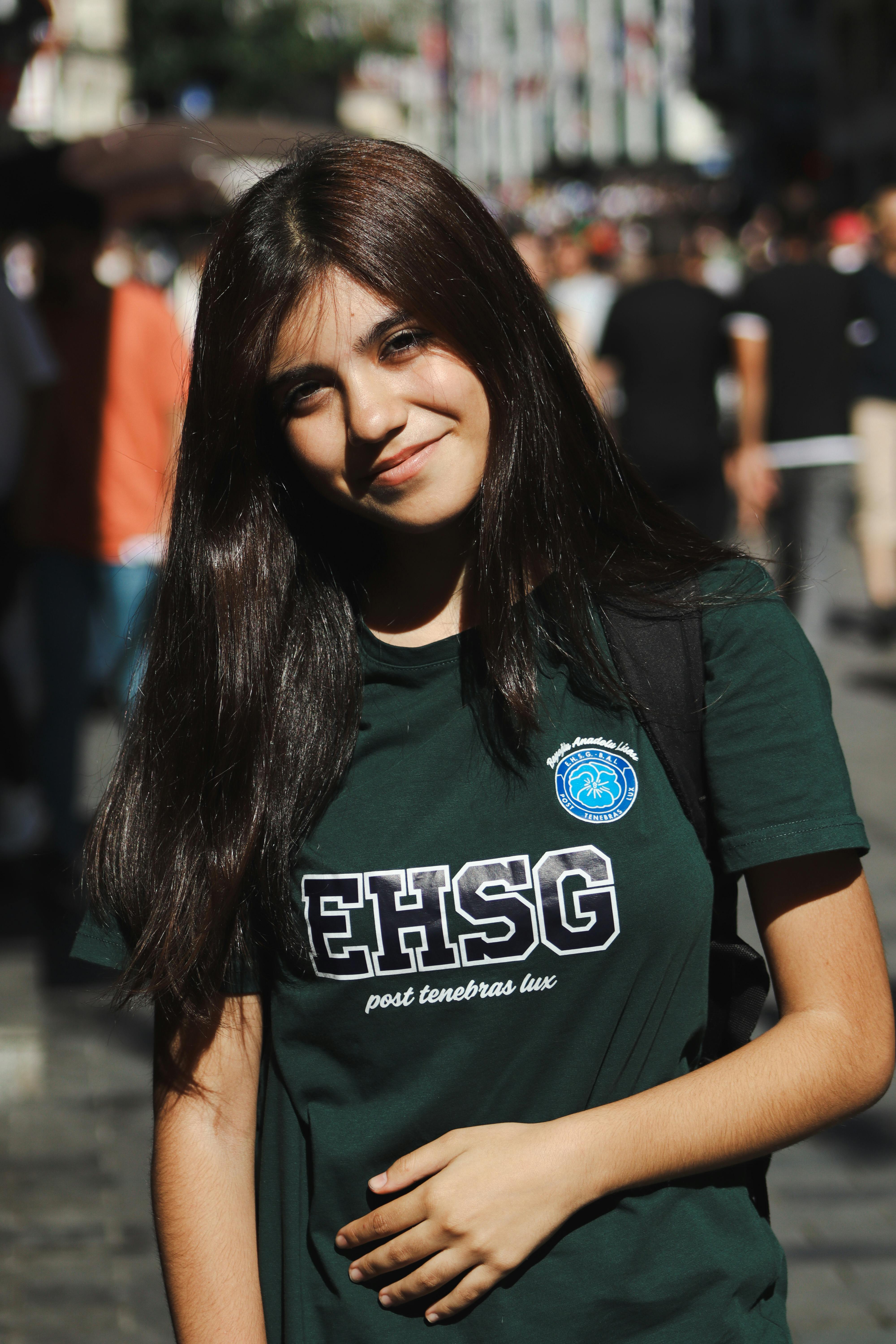 Portrait of a smiling woman in an urban environment wearing a green EHSG T-shirt.