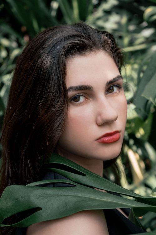 Free Close-up portrait of a woman with dark hair and red lips surrounded by green leaves Stock Photo