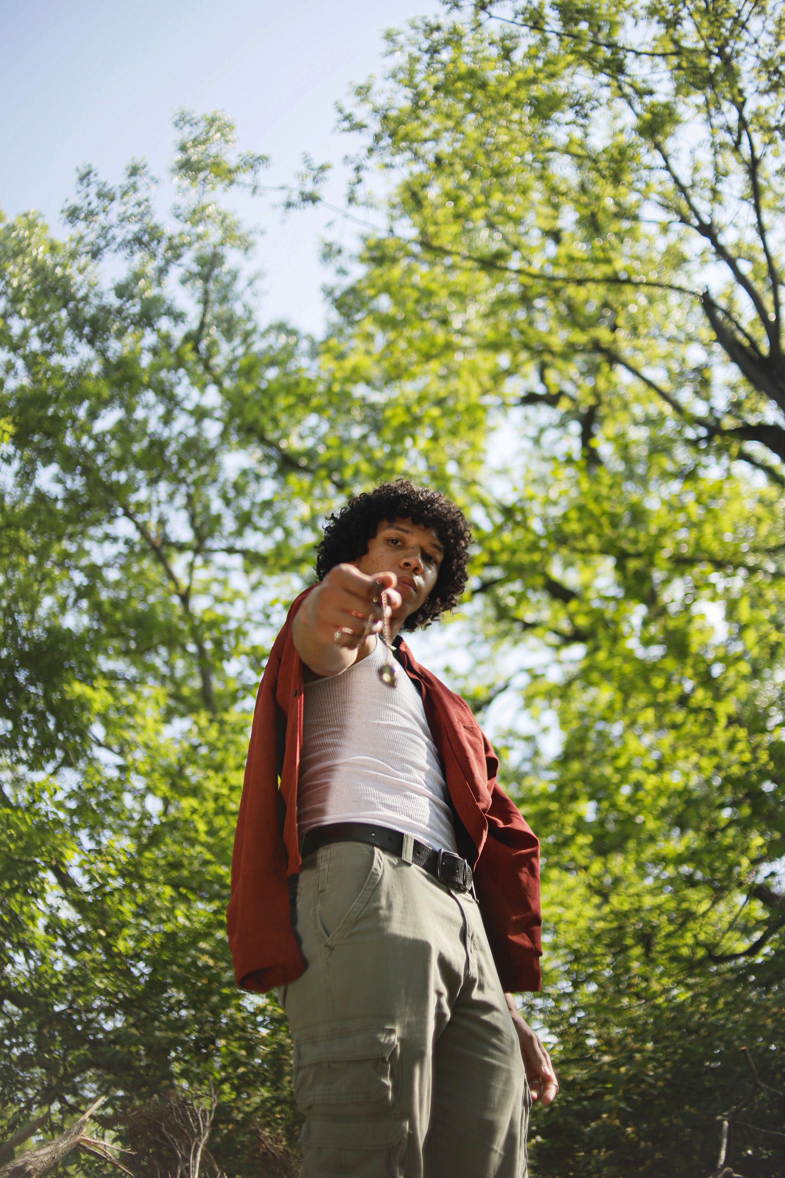 A fashionable adult man in an outdoor summer setting among lush trees captured from a low angle.