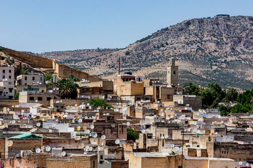Free Explore the vibrant rooftops of Fes with satellite dishes, against a backdrop of Moroccan mountains. Stock Photo
