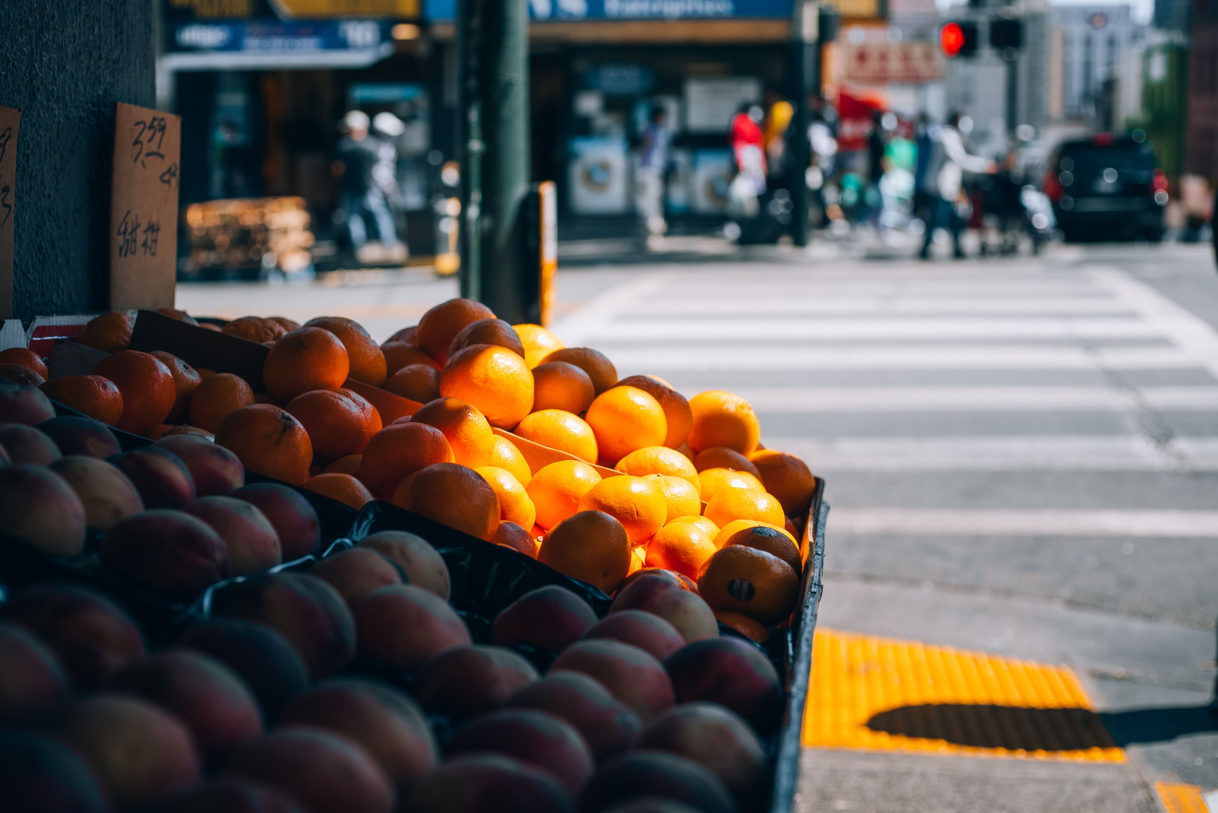 Fresh oranges and mangoes on a fruit stall along a busy urban crossing, capturing city life.