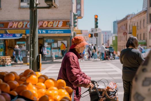 A bustling urban street market with people, oranges, and shops in the background.