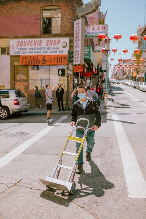 Free A man wearing a mask pushes a hand truck along a busy street adorned with red lanterns in Chinatown. Stock Photo